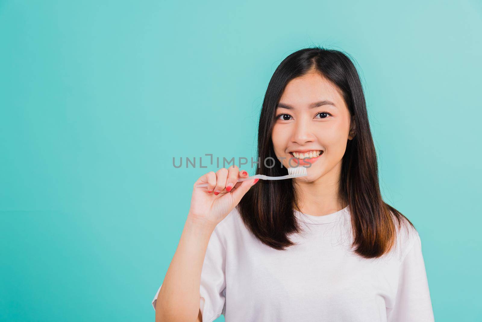 Asian beautiful young woman teen brushing teeth in the morning, portrait of happy Thai female confident smiling holding toothbrush, studio shot isolated on blue background, Dental health concept