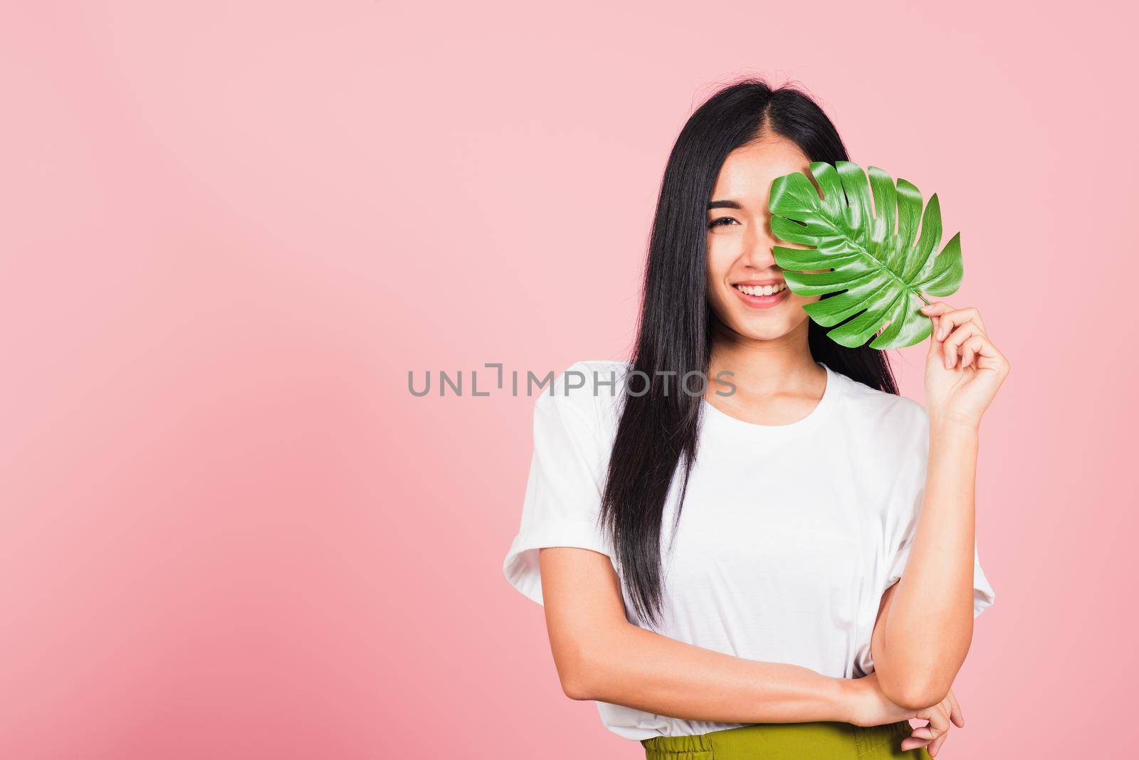 Beauty face. Portrait of Asian beautiful young woman with fresh healthy skin hold green monstera leaf on her face, Tropical Leaves, studio shot isolated on pink background, Skin body care spa concept