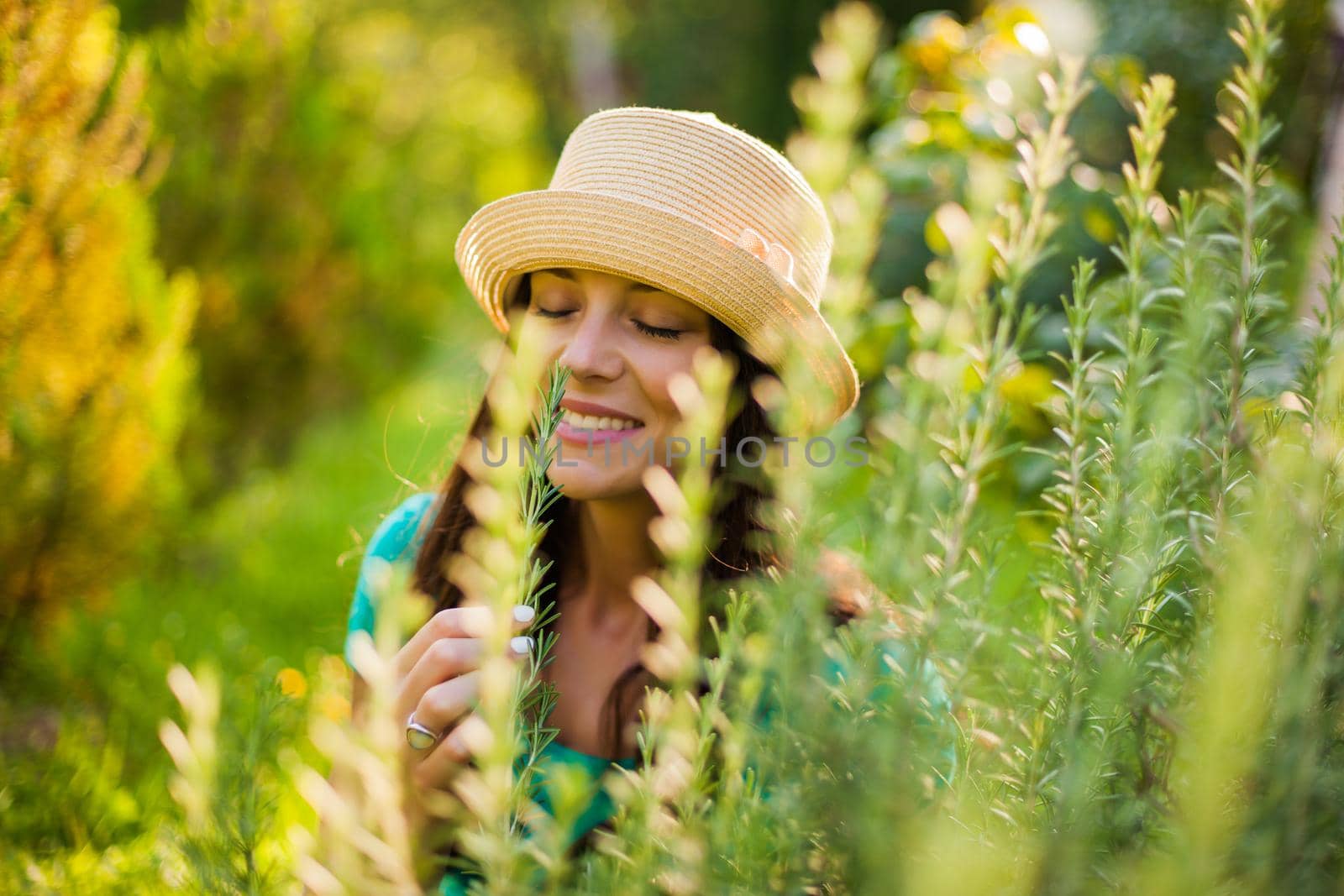 Young happy woman is enjoying the smell of rosemary in her garden.