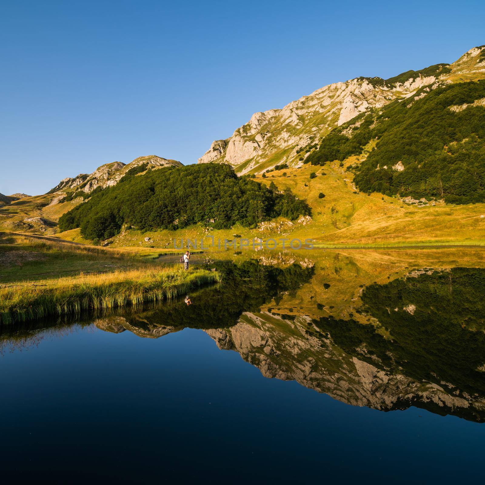 Photographer taking photo on mountain lake in summer.