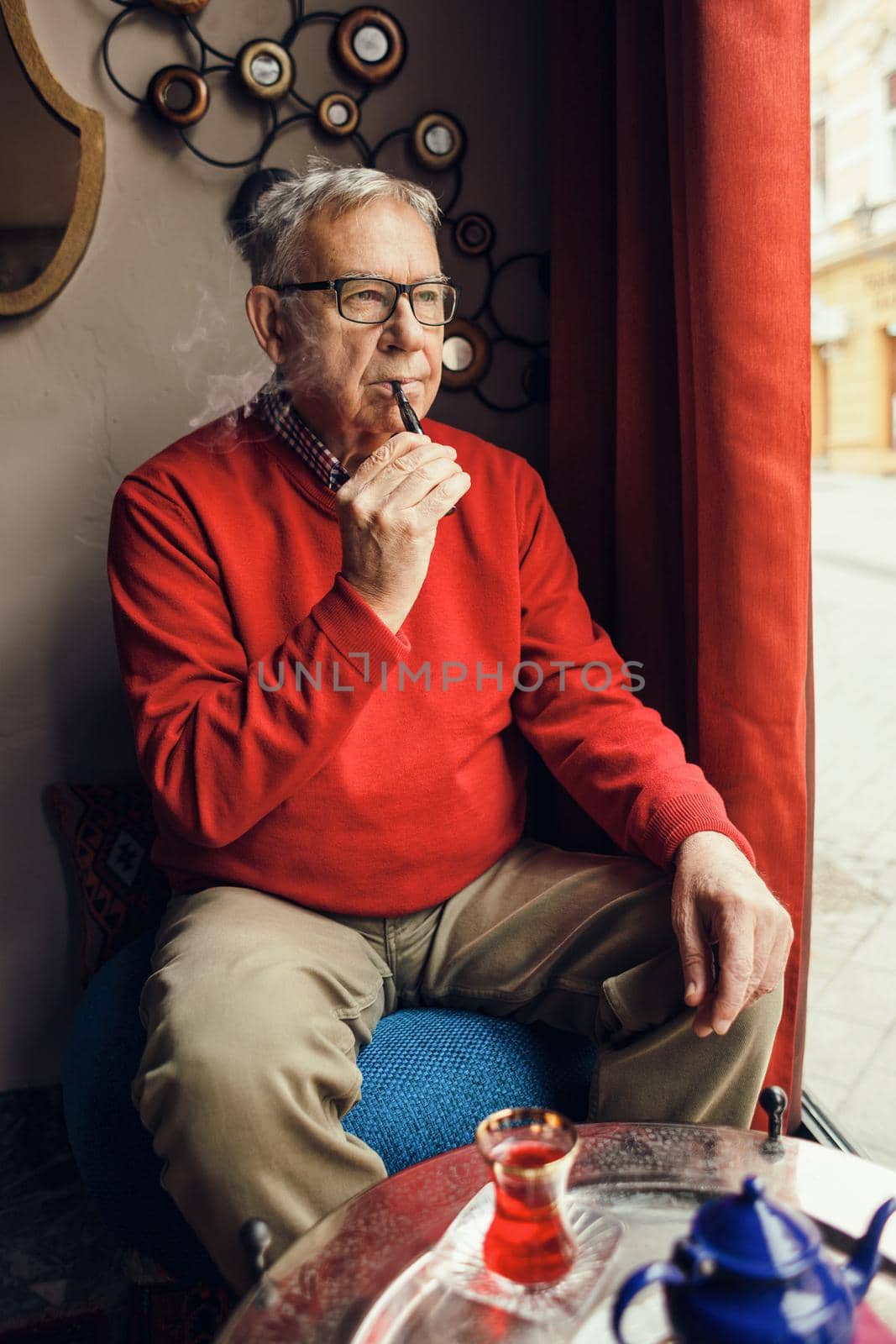 Senior man is sitting in cafe and smoking electronic cigarette.