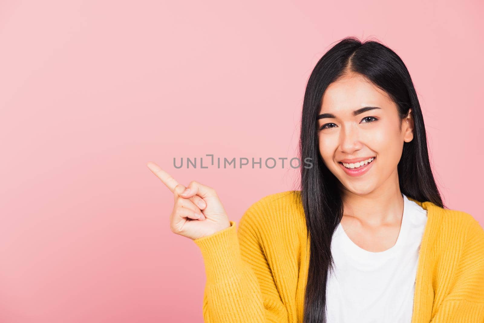 Happy Asian portrait beautiful cute young woman standing smiling indicate finger empty space looking to camera, studio shot isolated on pink background, Thai female pointing index out with copy space