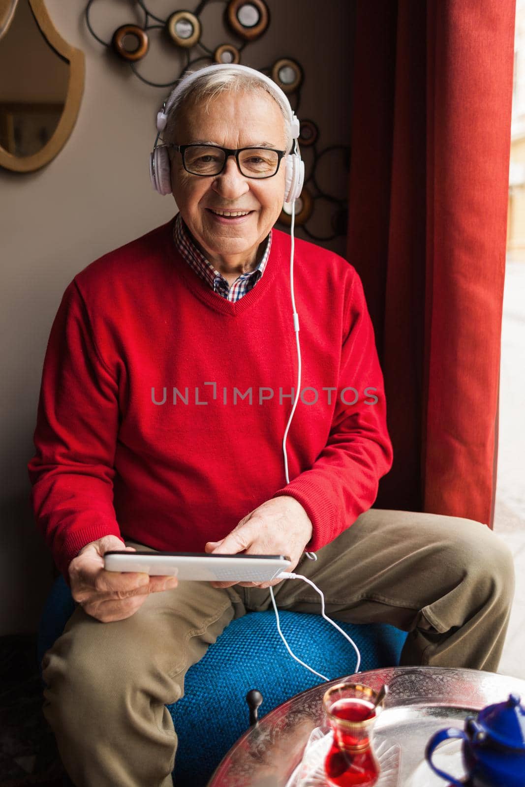 Portrait of happy senior man who is chatting on digital tablet in a cafe.