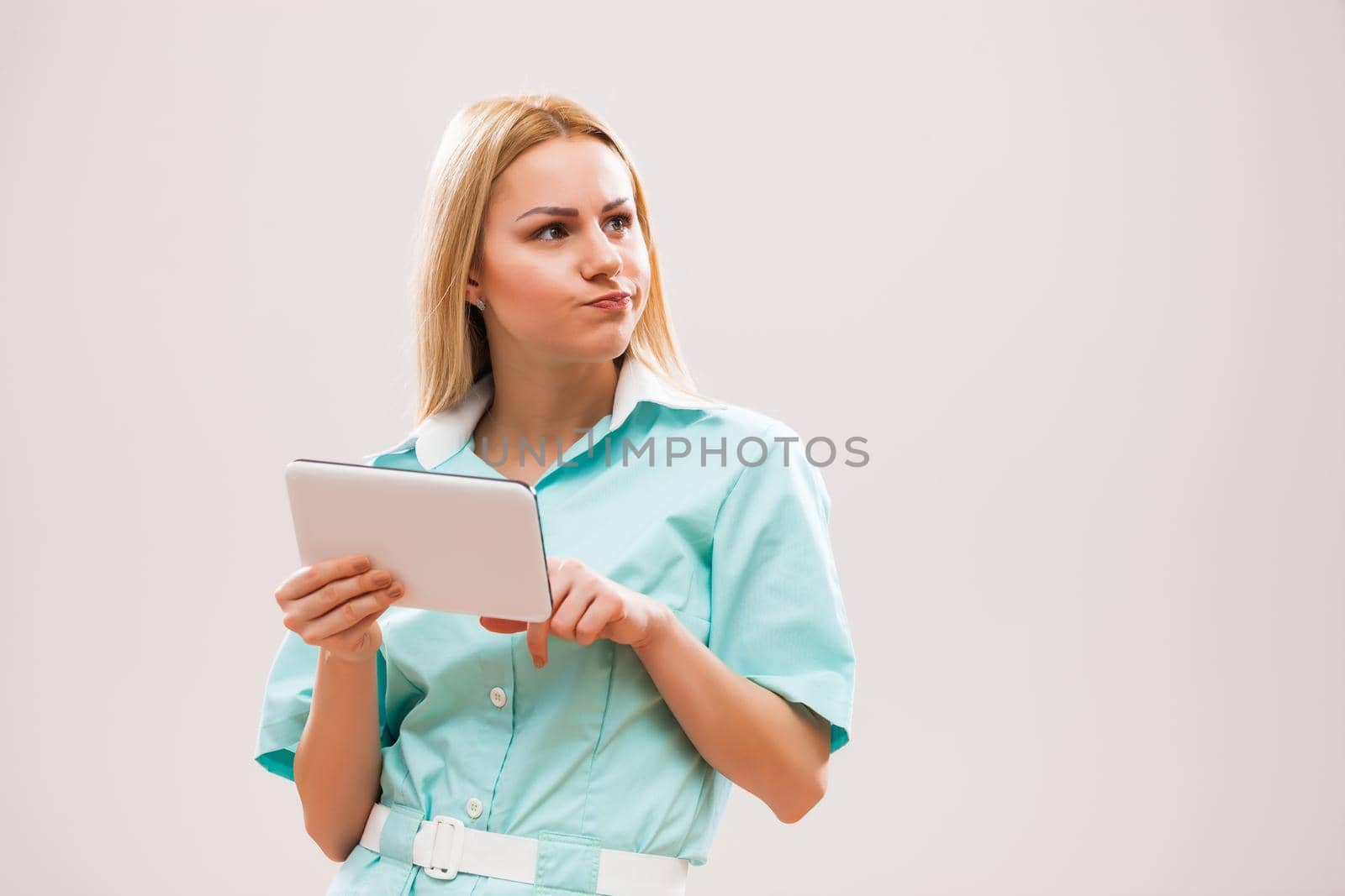 Portrait of young nurse who is examining therapies on digital tablet.