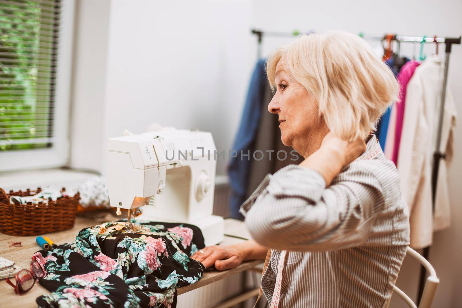 Adult woman is sewing in her studio. She is tired and having pain in her back.