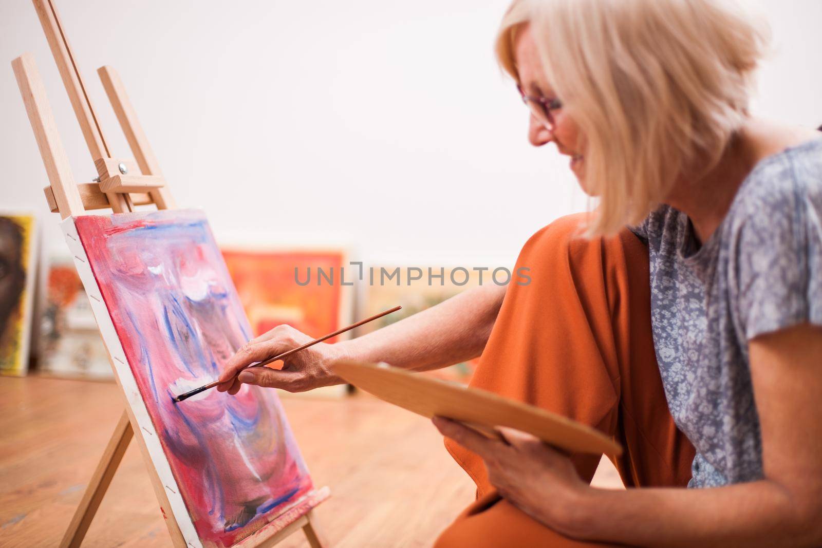 Elderly woman is painting in her home. Retirement hobby.