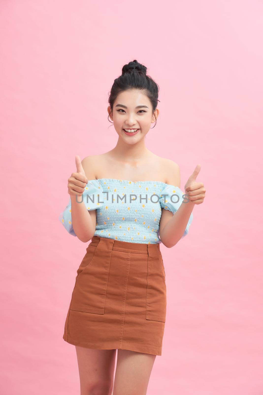 Pretty asian woman standing over pink background smiling and doing the ok signal with her thumbs by makidotvn