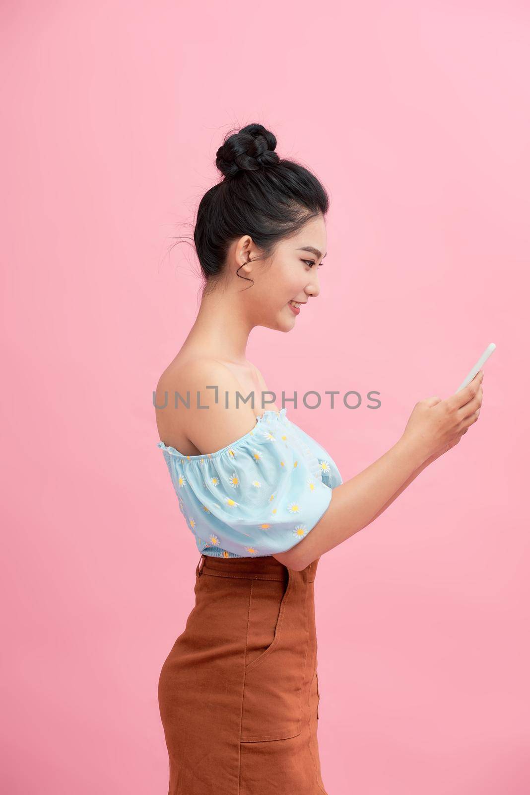 Dreamy asian beauiful young woman holds modern electronic device, isolated over pink background. by makidotvn