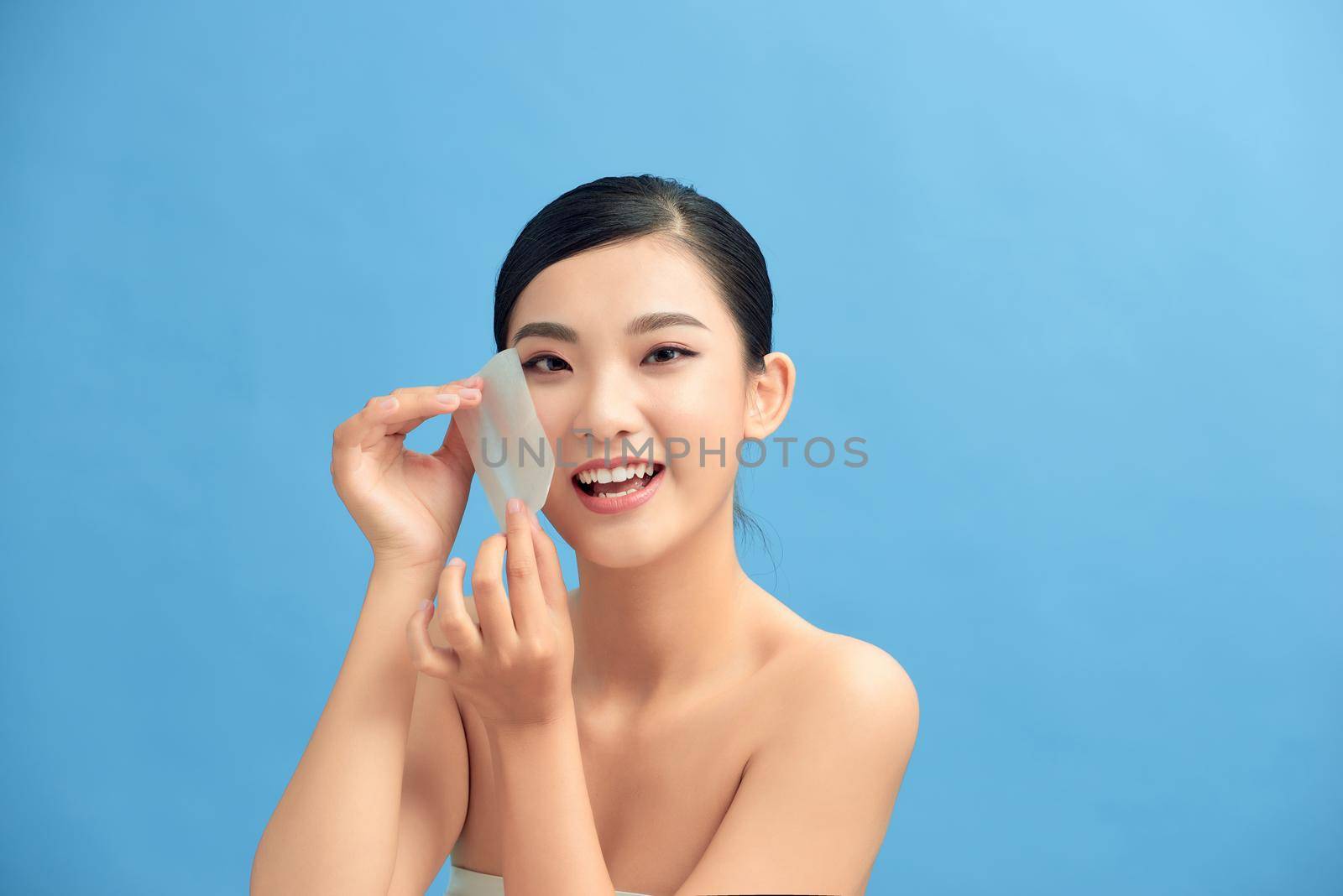 Beauty treatment and skin care. Beautiful Asian model using absorbing sheet.
