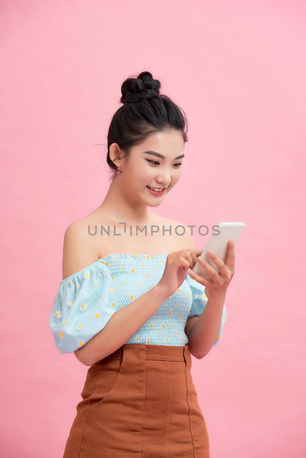 Excited Asian girl using smartphone standing over pink background. Empty Space by makidotvn