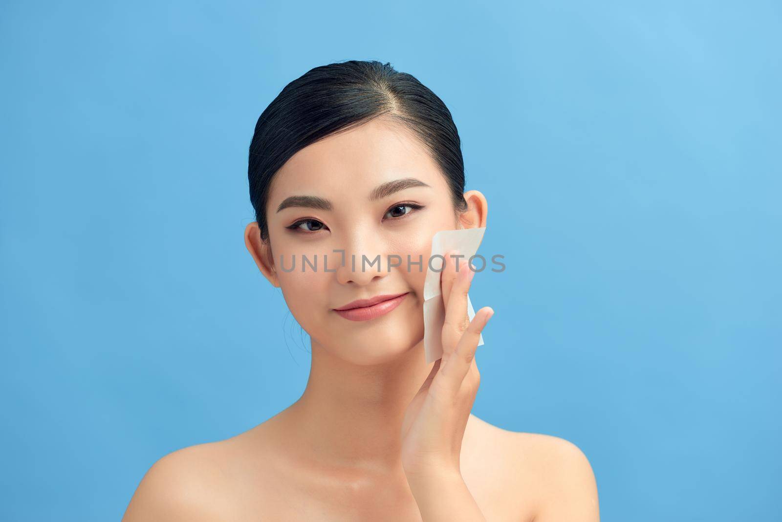 Skin care. Young woman removing oil from face using blotting papers.  by makidotvn