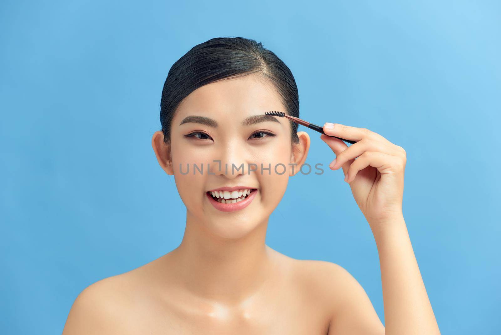 Closeup beautiful woman with eyebrow brush tool on blue by makidotvn