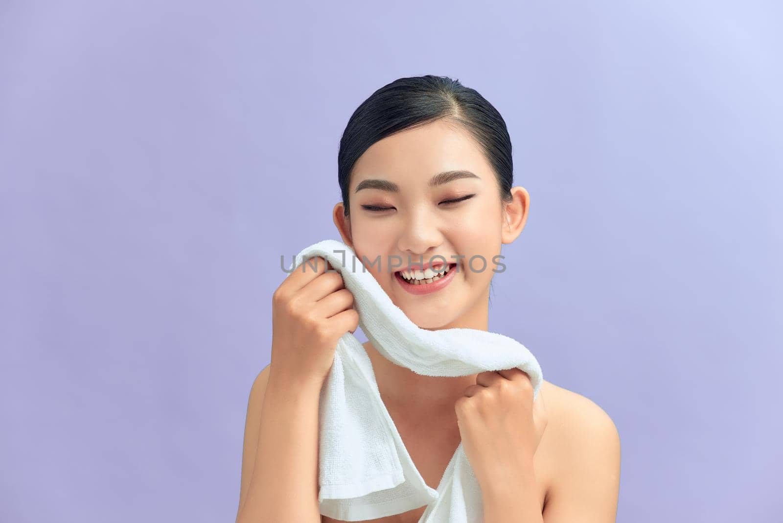Beautiful happy smiling young asian female model wiping facial skin with soft towel, removing makeup by makidotvn