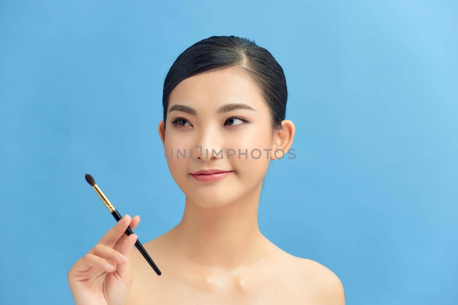 Beautiful woman using brush for eyeshadow. Photo of woman with perfect makeup on blue background. Beauty concept