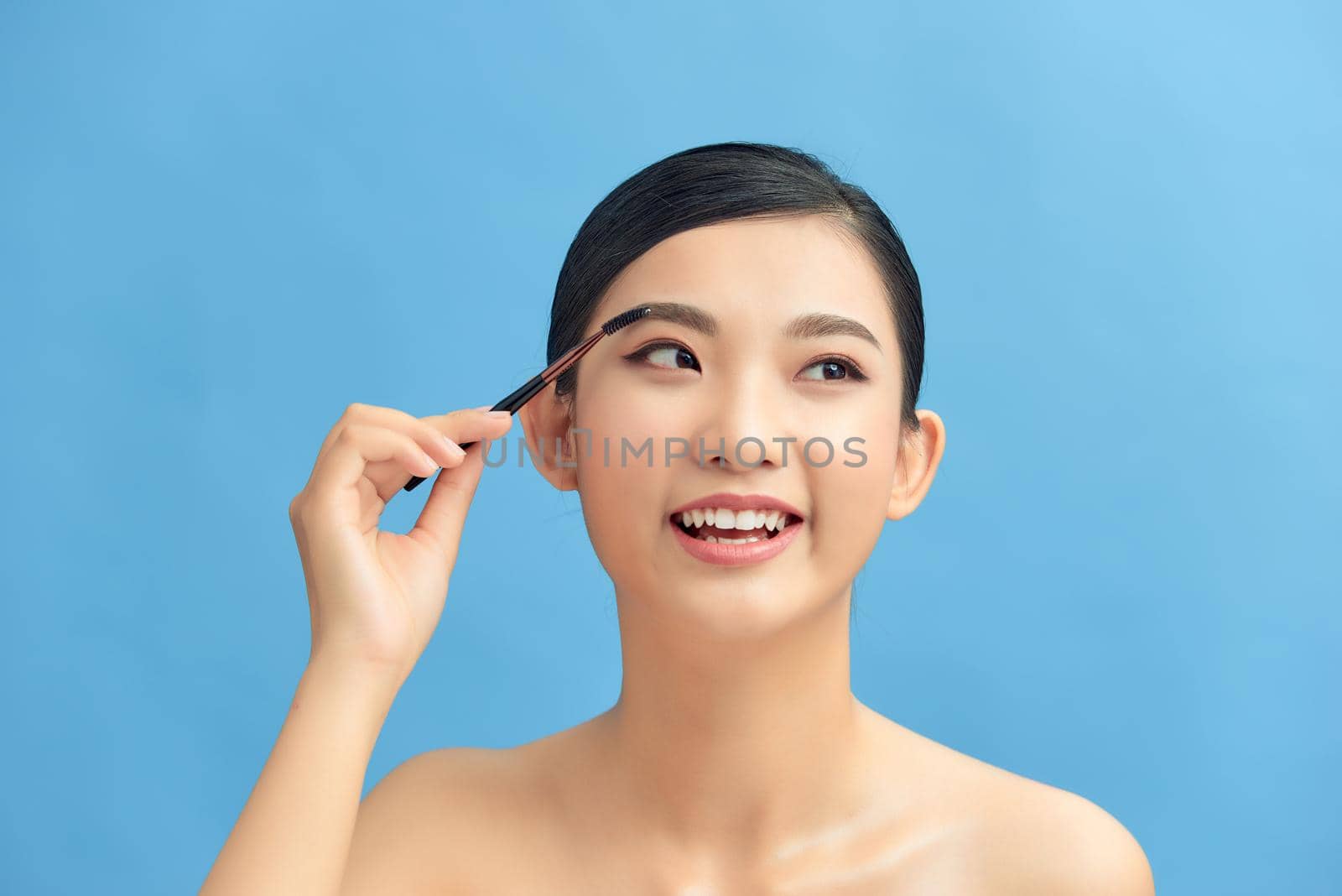 Beautiful woman using brush for eyeshadow. Photo of woman with perfect makeup on blue background. Beauty concept by makidotvn