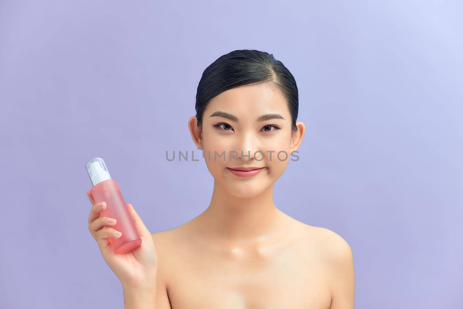 Portrait of a beautiful young girl standing isolated over color background, showing body lotion bottle