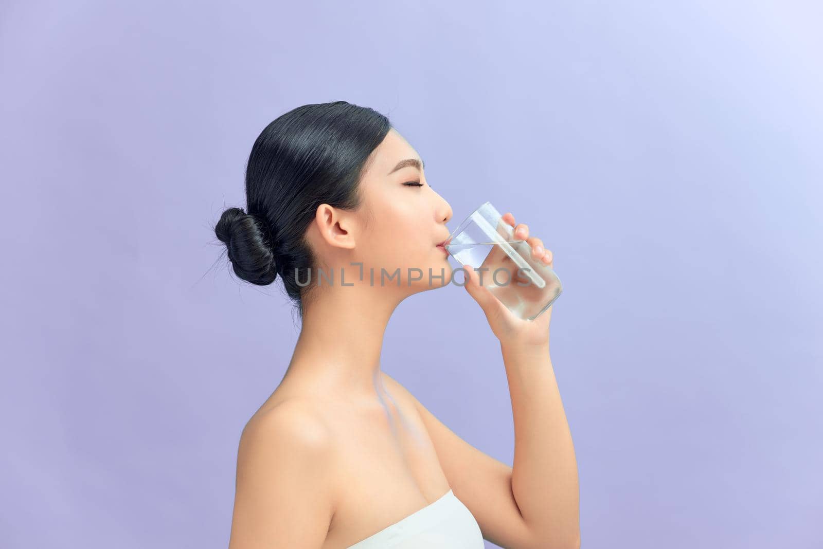 Attractive woman drinking water against purple background by makidotvn