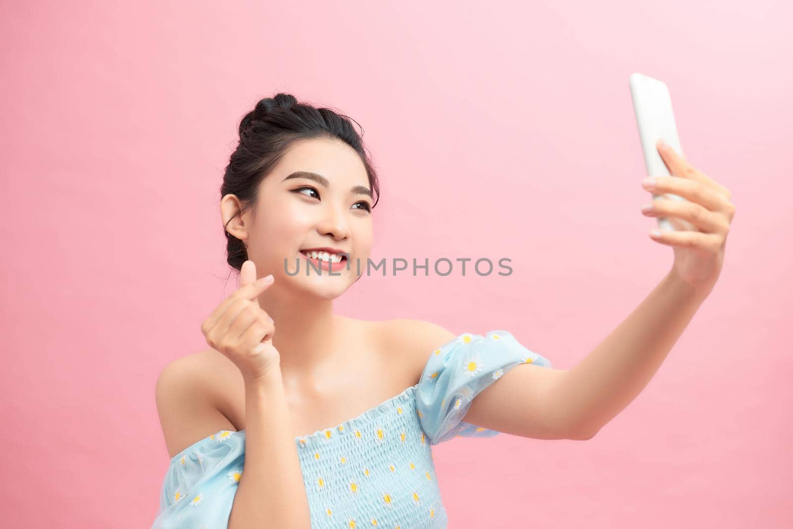 Image of stylish girl showing heart sign and mobile phone screen, like something online, standing over pink background by makidotvn
