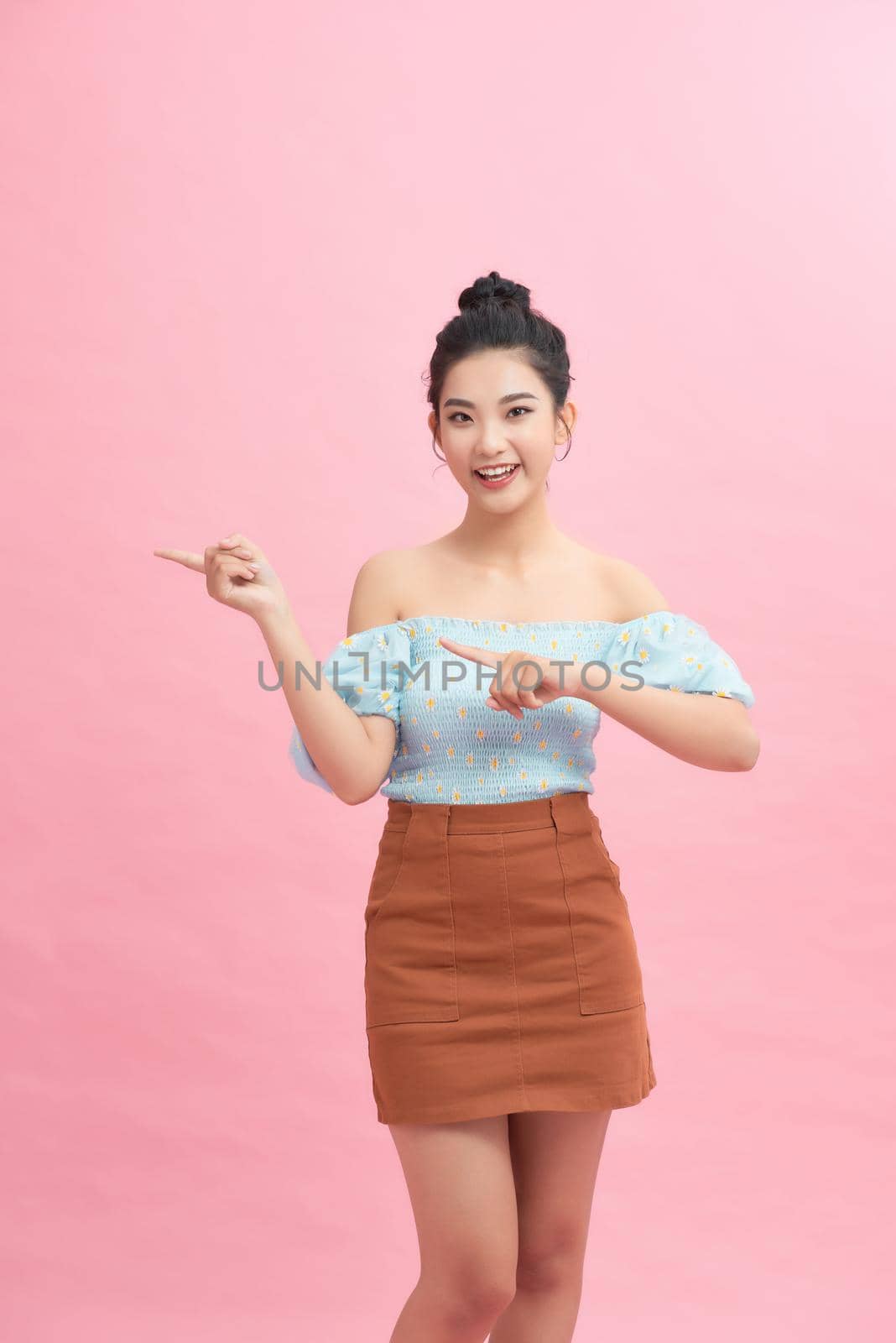 Beautiful asian woman pointing to copy space. isolated on pink background. by makidotvn