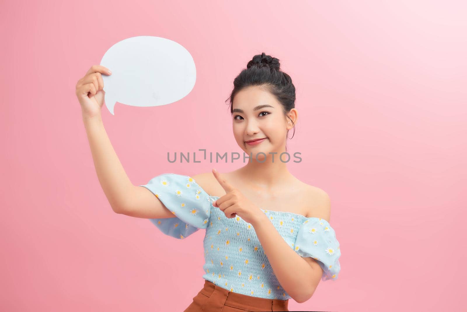 Portrait of an excited young woman holding empty speech bubble and pointing finger up isolated over pink background by makidotvn