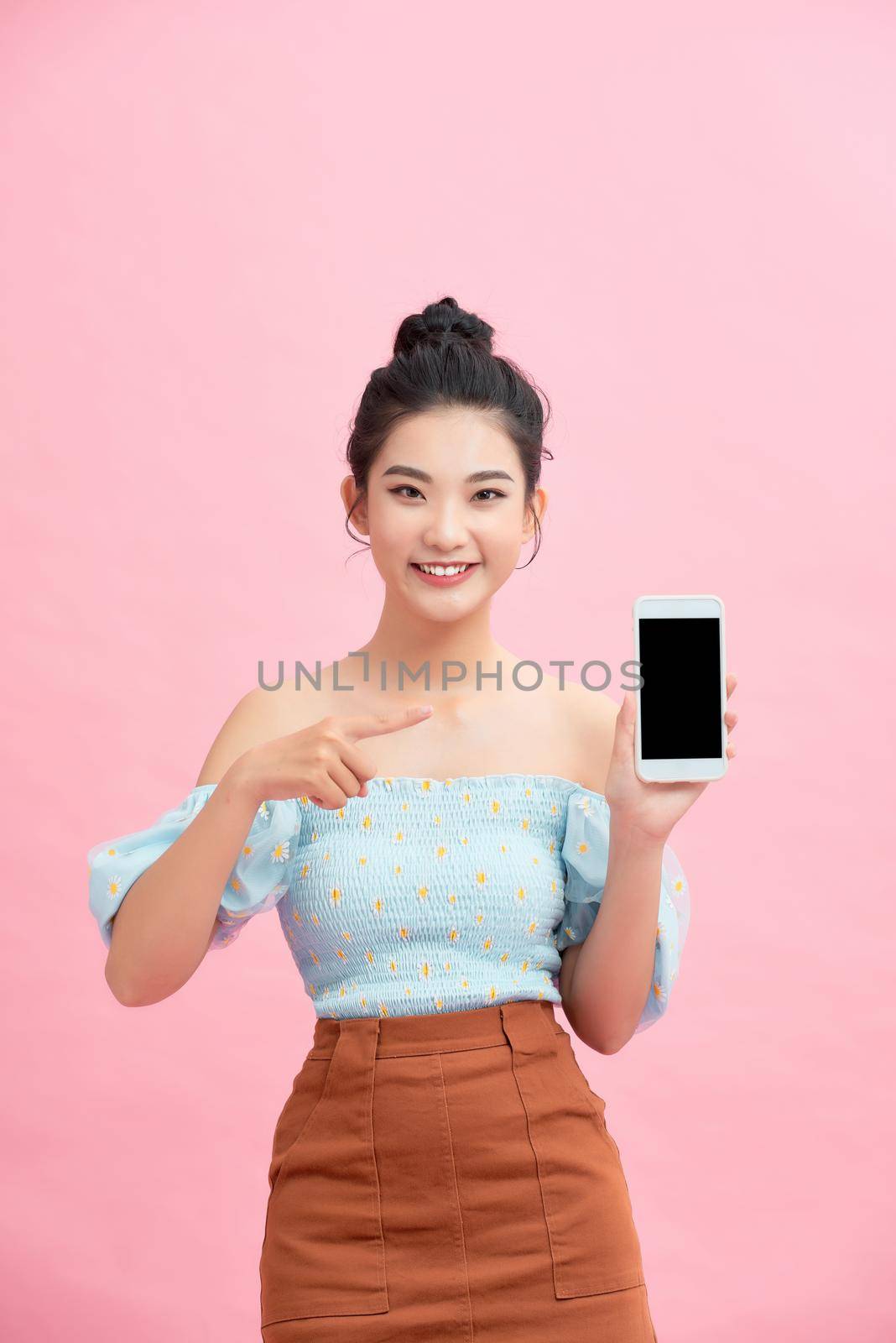 Portrait of an excited young woman showing blank screen mobile phone isolated over pink background by makidotvn