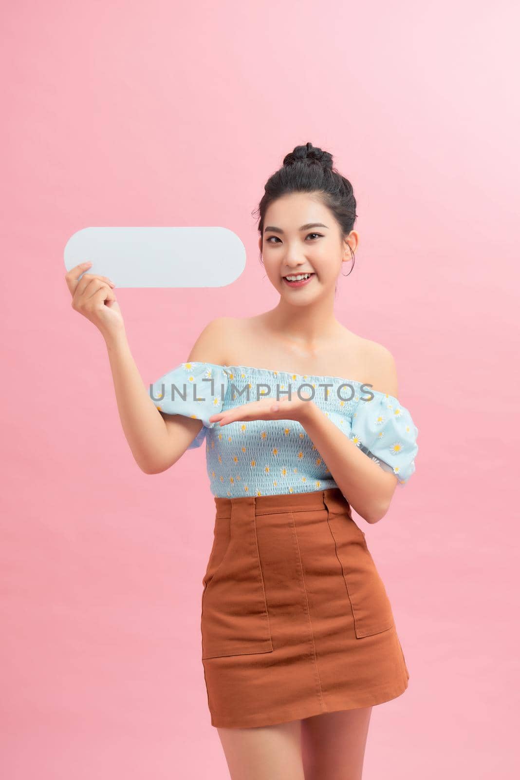 Portrait of young girl holding blank text bubble in specs isolated over pink background