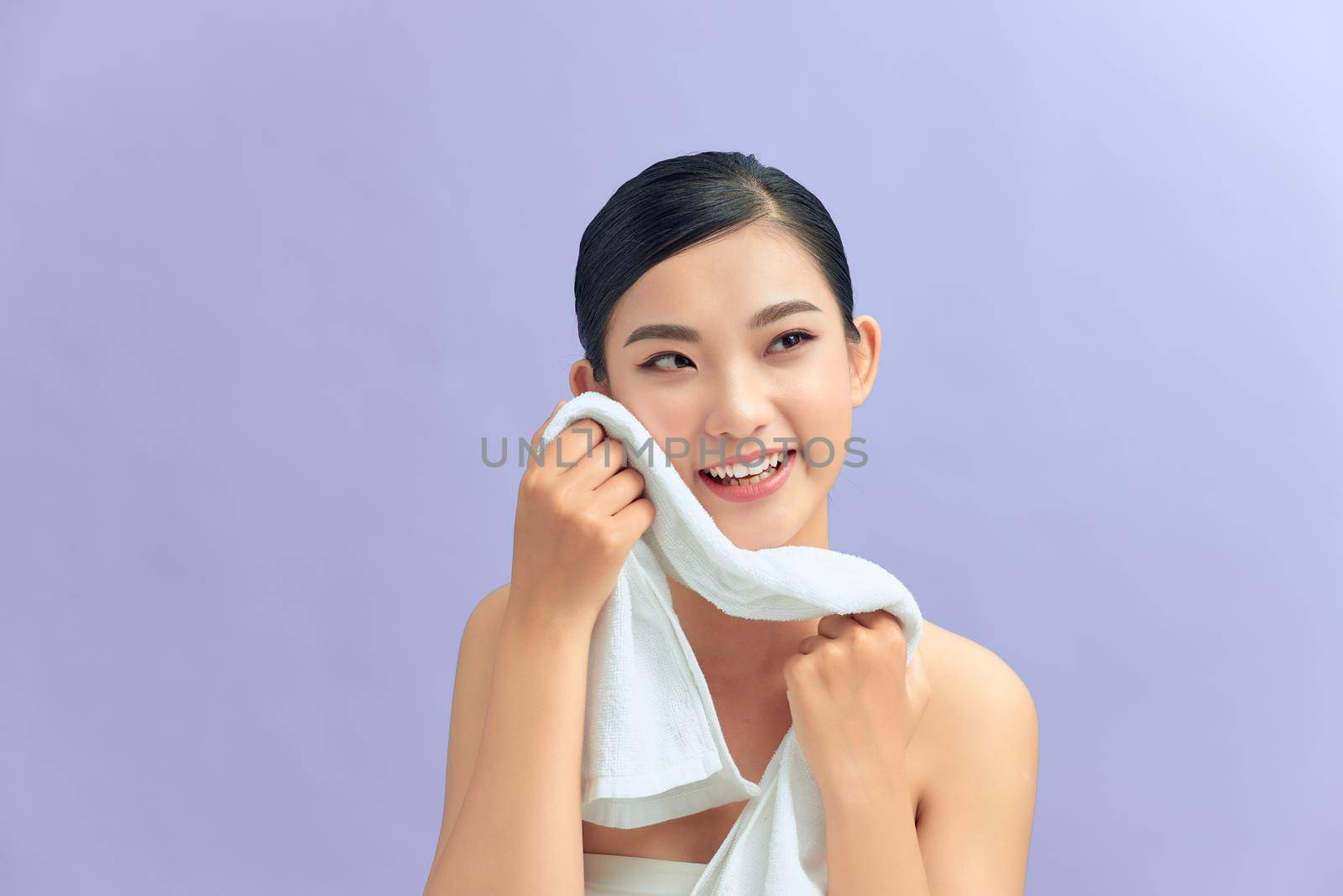 Beautiful happy smiling young asian female model wiping facial skin with soft towel, removing makeup