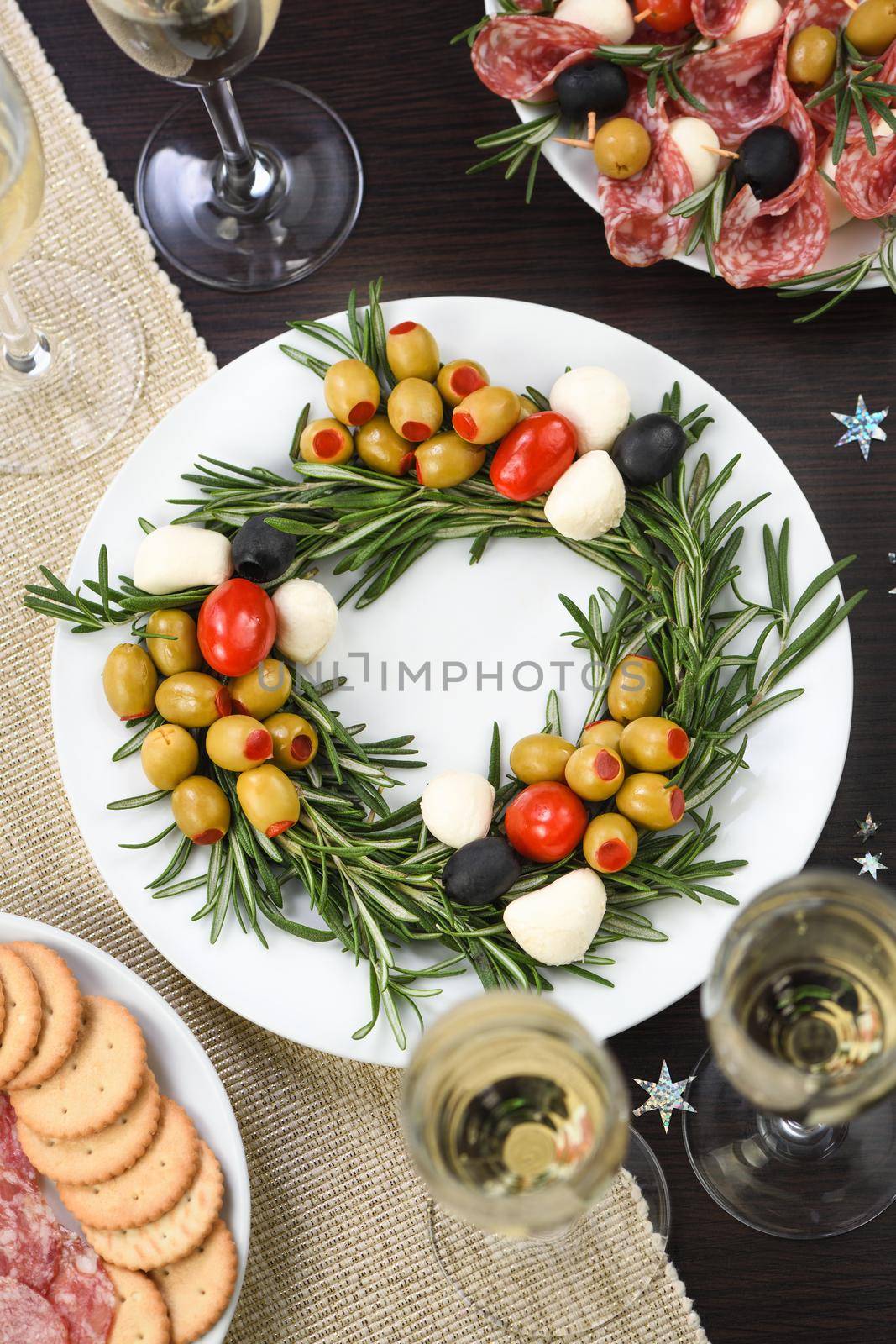 An appetizer of rosemary stuffed with olives with baby mozzarella and cherry tomatoes. Made in the form of a Christmas wreath.