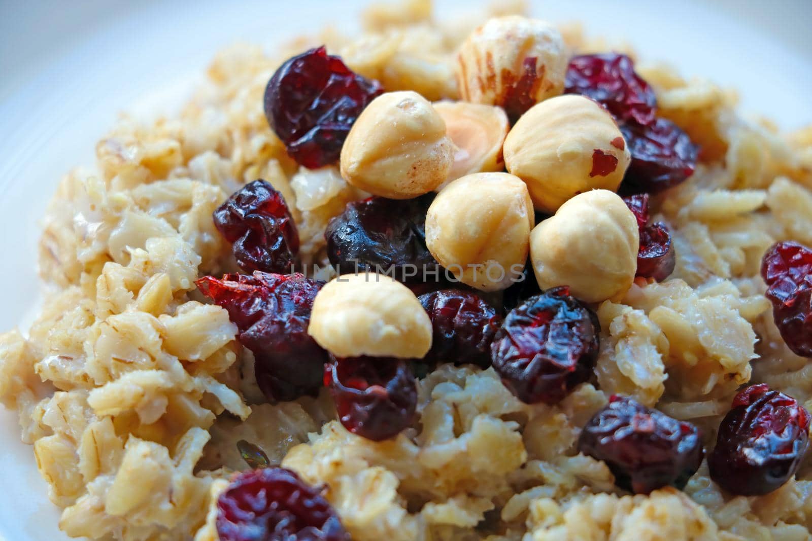 Plate with cooked oatmeal, hazelnuts and cranberries. Healthy food