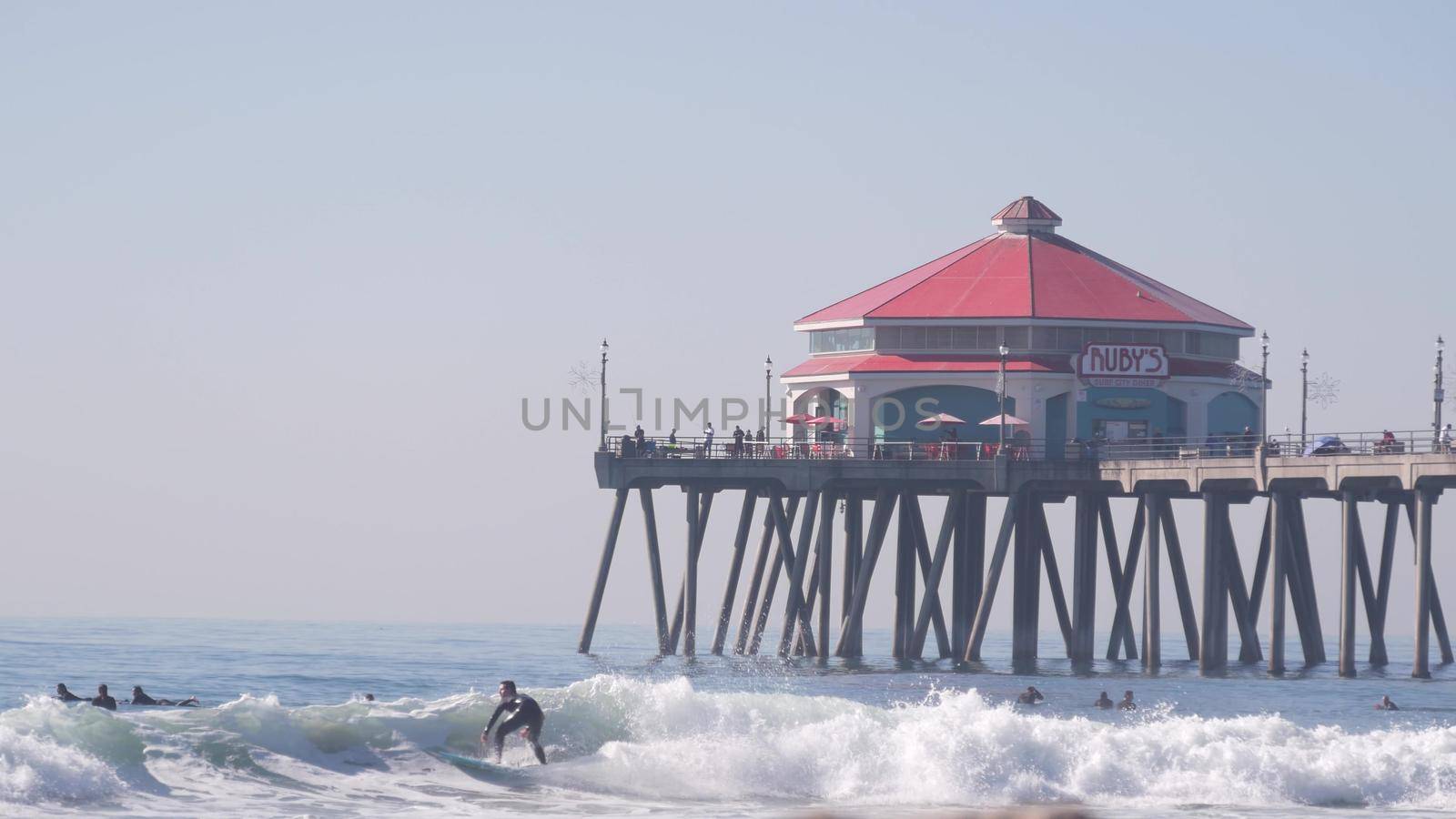 People surfing in ocean waves, Huntington Beach pier, California coast, USA. by DogoraSun