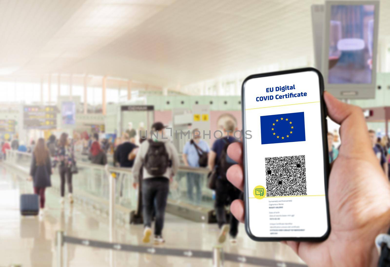 EU Digital COVID Certificate with the QR code on the screen of a mobile held by a hand with blurred airport in the background by rarrarorro