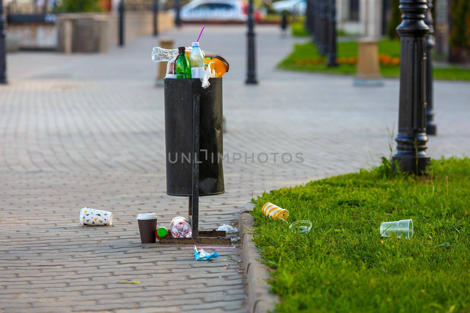 overflowing trash can on the sidewalk pavement at summer daylight.
