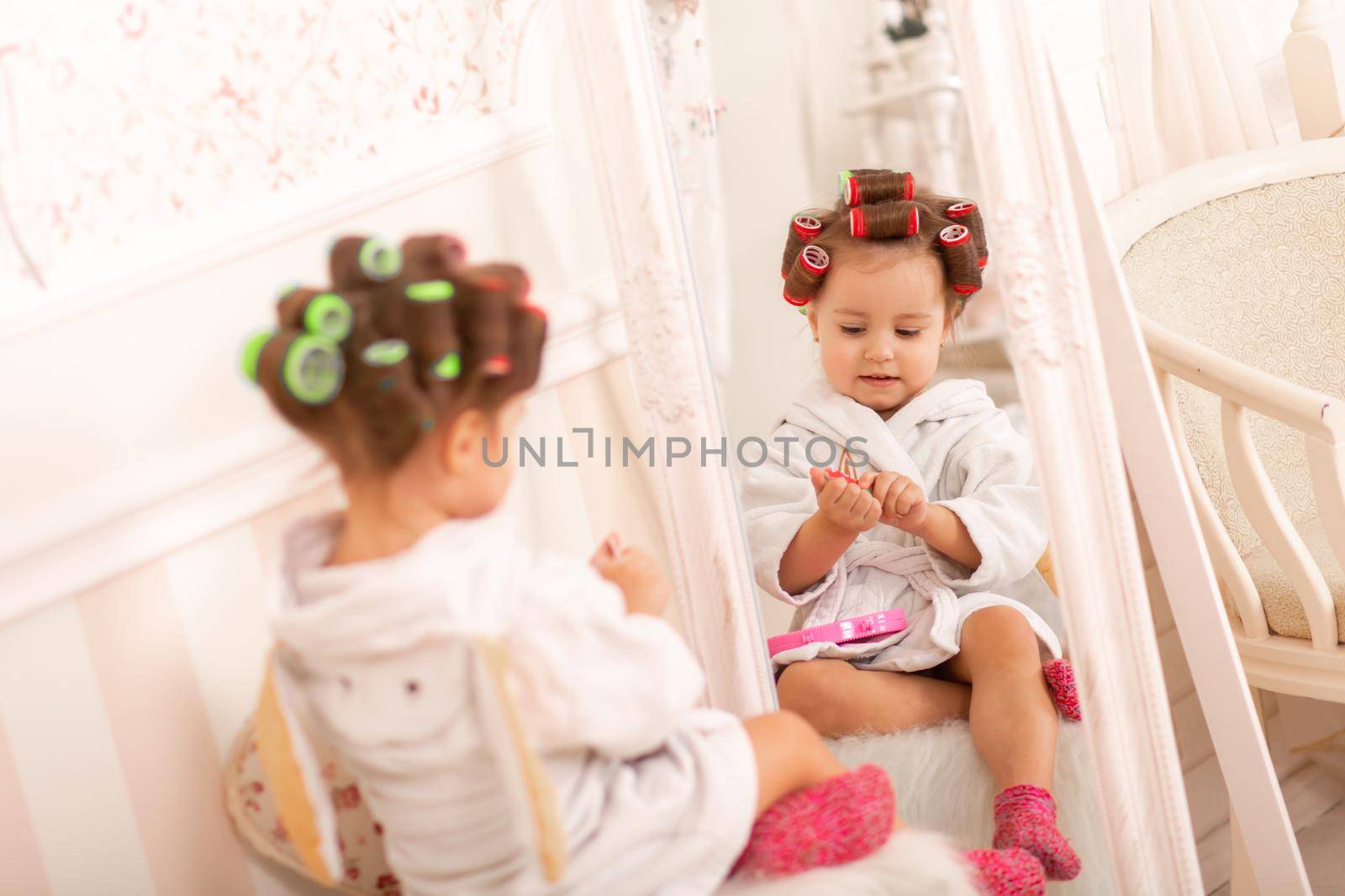 Adorable little girl with curlers paints her fingernails. Copies mom's behavior. Young fashionista. Beauty day.