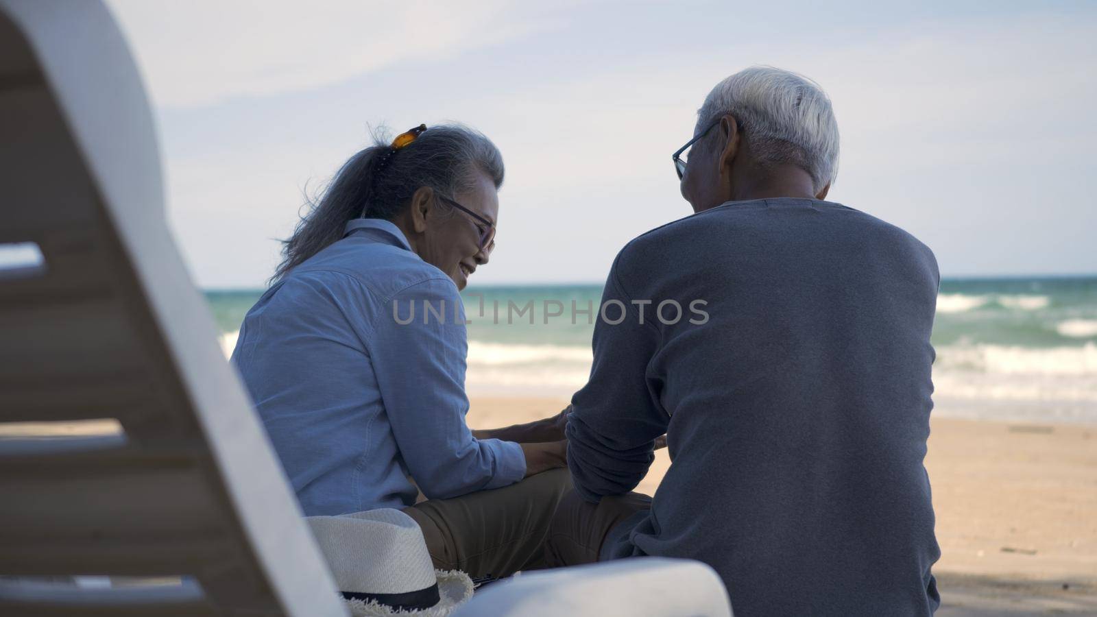 Happy Asian family, senior couple sitting on chairs with backs on beach travel vacation talking together by Sorapop