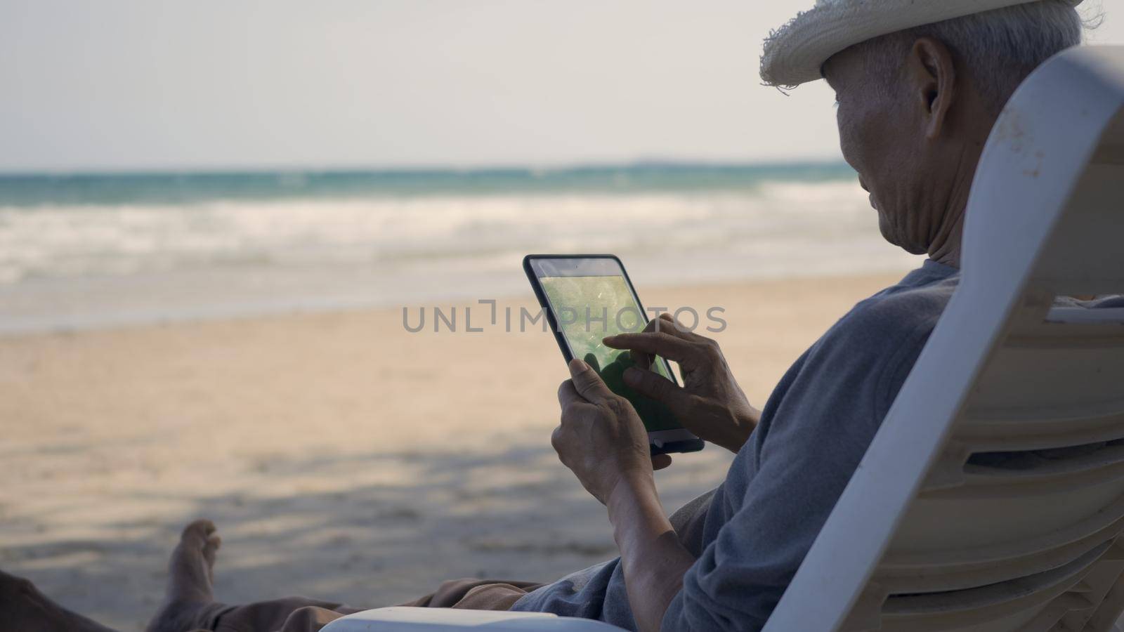 Senior man sitting on chairs enjoying time on beach travel vacation using tablet computer by Sorapop