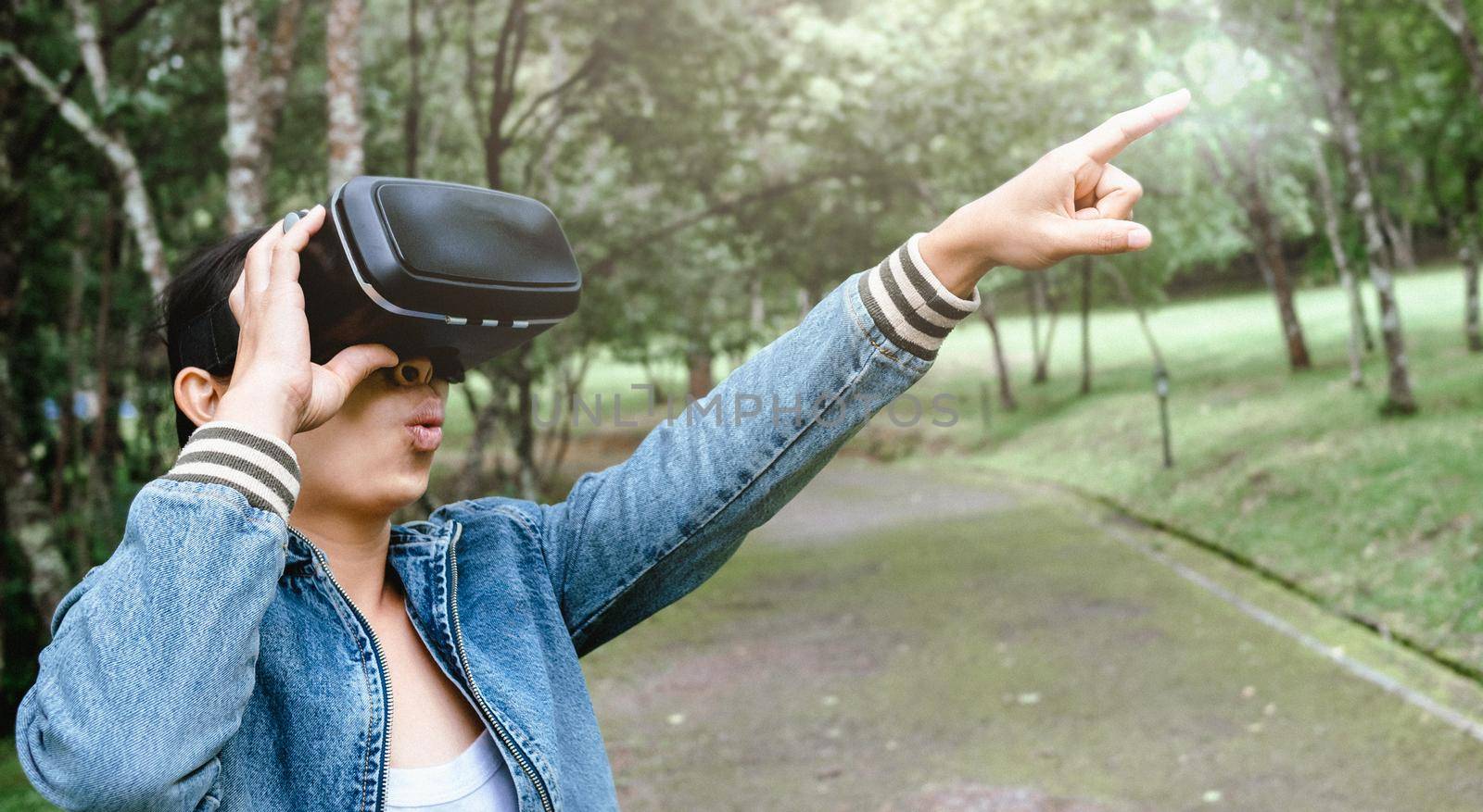 Happy woman wearing VR-headset glasses of virtual reality in forest and enjoying the nature on a sunny summer day in spring garden. Modern technology concept. by TEERASAK