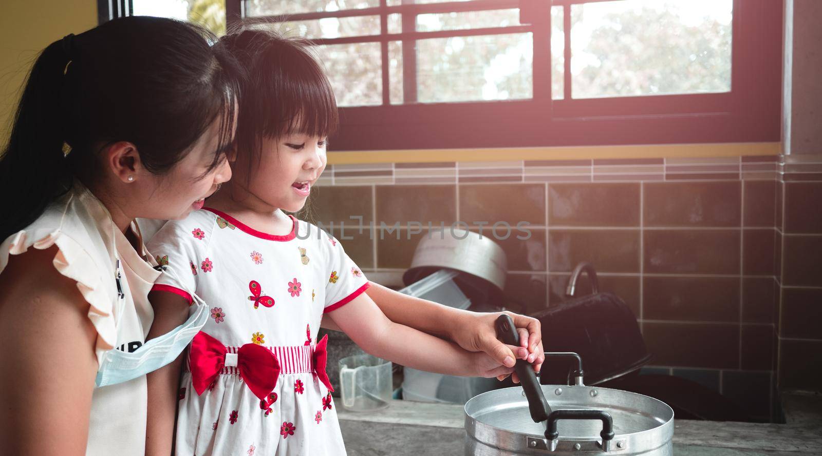 Mother holds her daughter's hand with a ladle to melt the boiling gelatin in a pot on the kitchen gas stove. A mother is teaching her daughter to make jelly ay home.