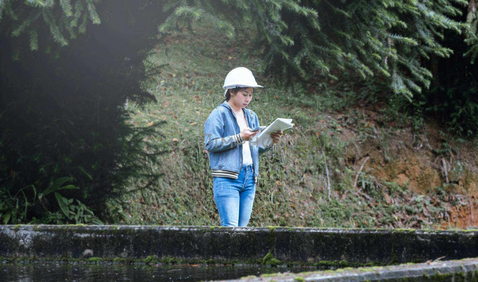 Female ecologist in safety hat working and controlling a quality of water at wastewater treatment plant. Environmental engineers working at water recycling plant for reuse.