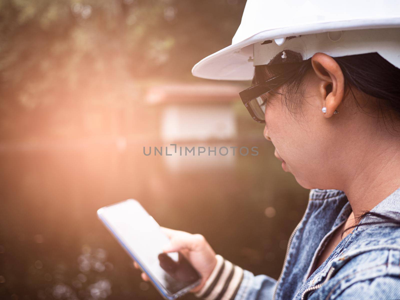Female ecologist in safety hat working with a smart phone and controlling a quality of water at wastewater treatment plant. Environmental engineers working at water recycling plant for reuse. by TEERASAK