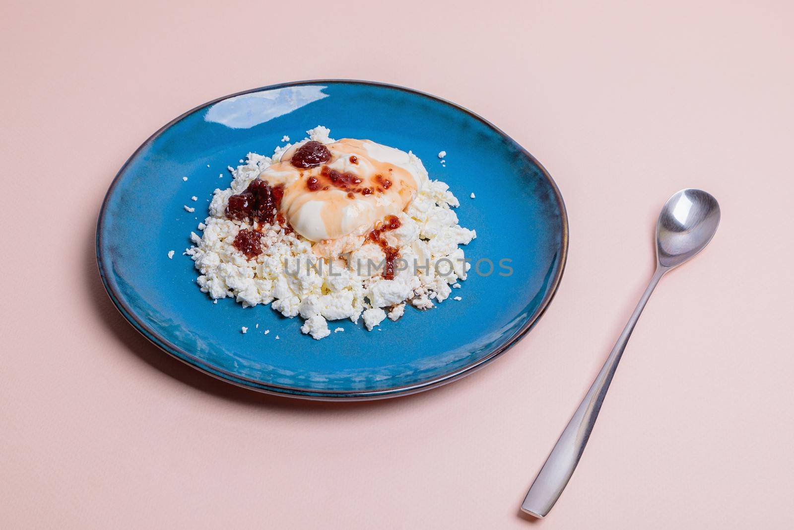 Blue plate with cottage cheese and jam on a pink background. Morning breakfast concept.
