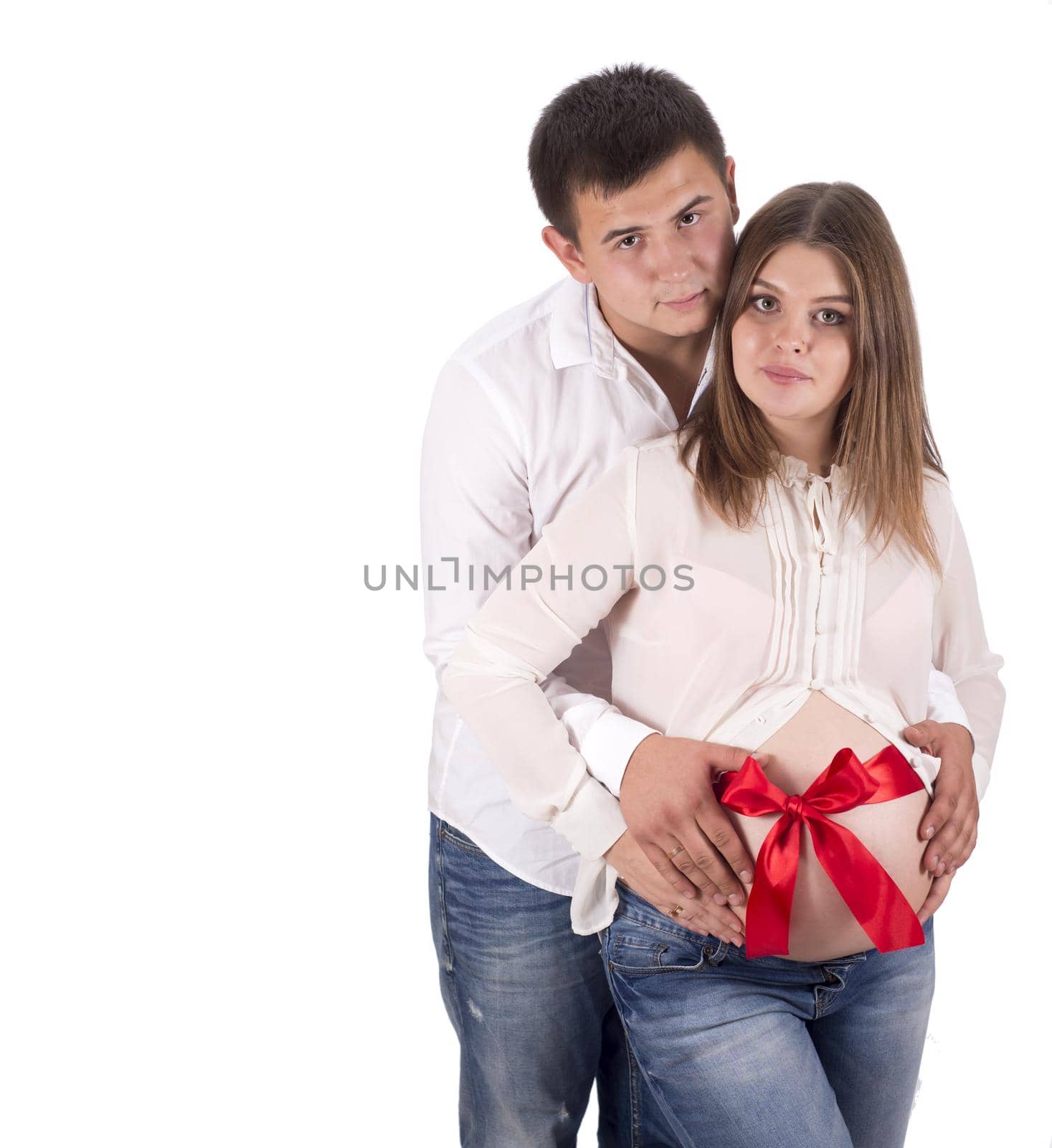 A man and a pregnant woman in jeans and white shirts. Red ribbon tied around the belly of a pregnant woman on white background by aprilphoto