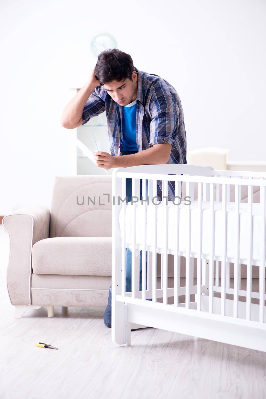 Young man assembling baby bed with instruction manual