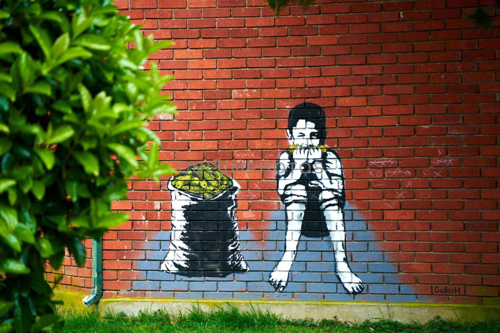 Graffiti drawing on a brick wall. A boy eats corn while sitting near a sack full of corn.