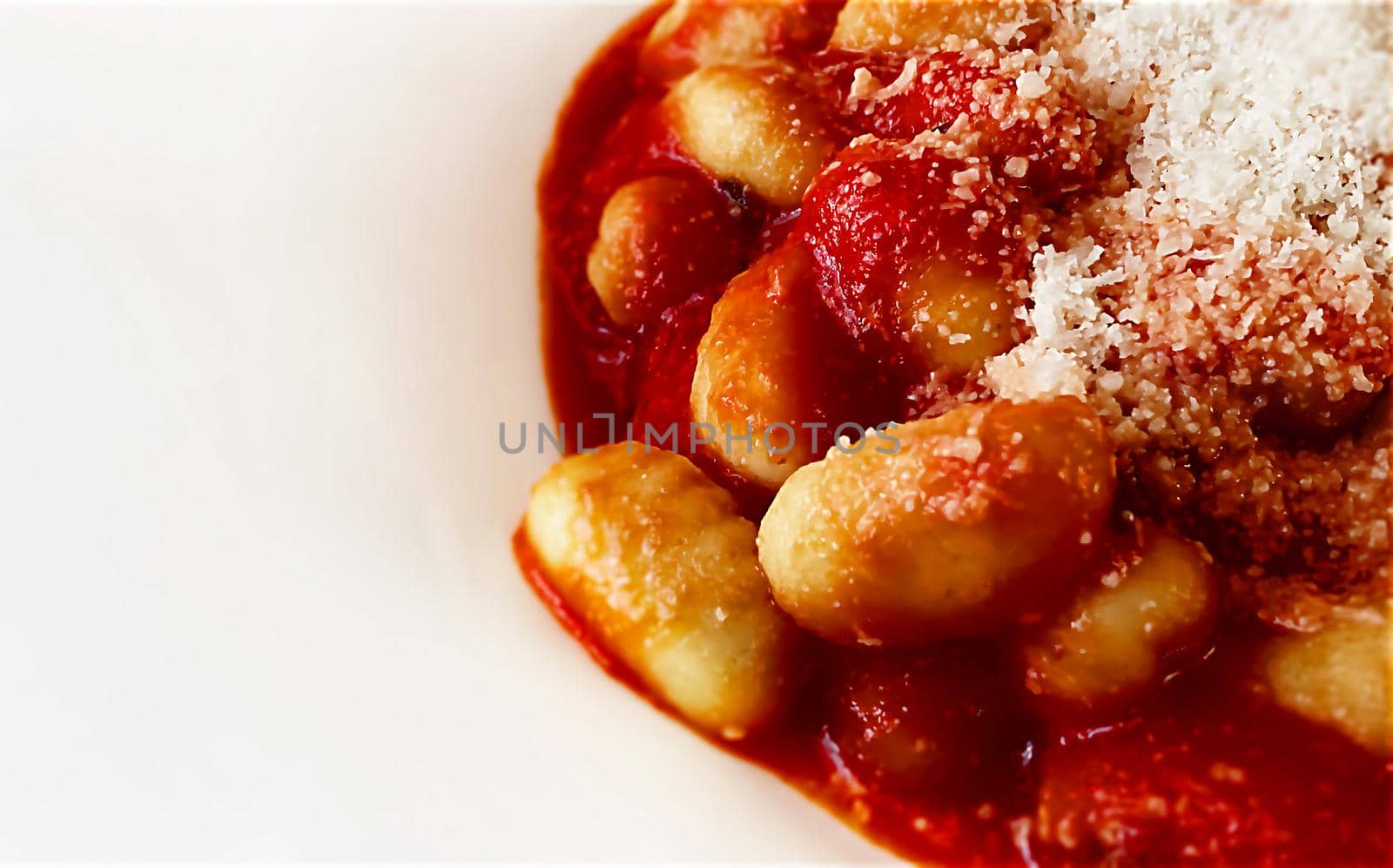 Close up of a portion of gnocchi in tomato sauce with grated parmesan cheese served in a white ceramic plate. Italian food and cuisine.