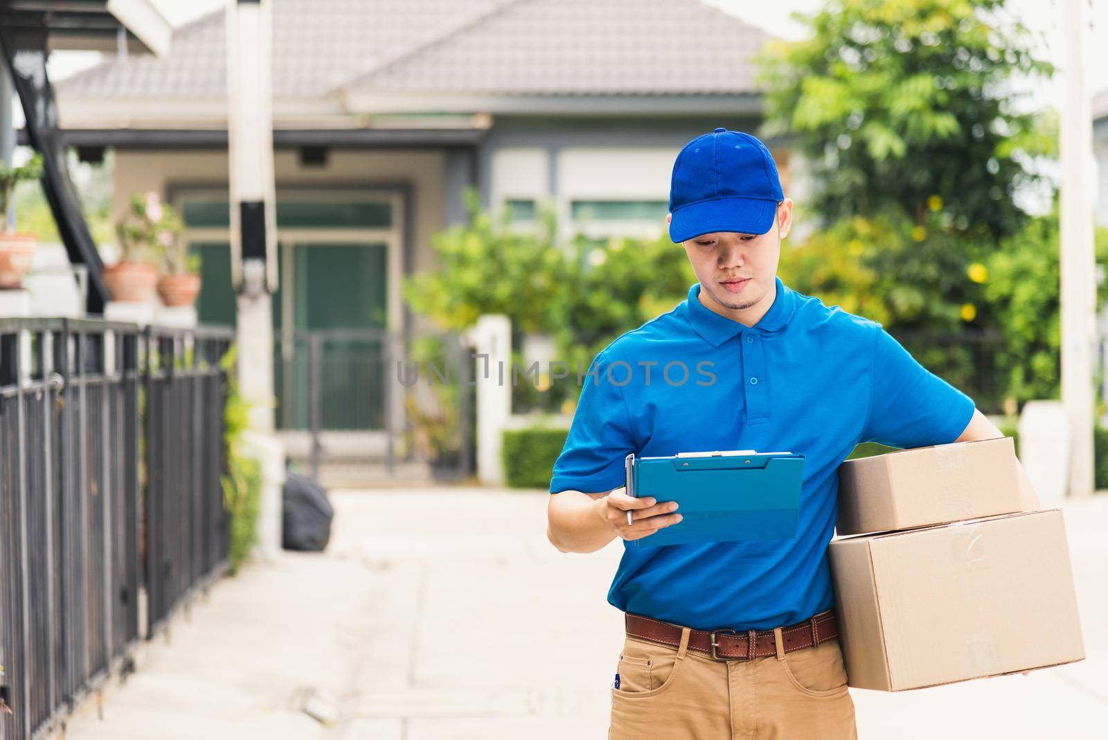 delivery man courier in uniform hold parcel post boxes service shipment and walking finding and looking for customer home by Sorapop