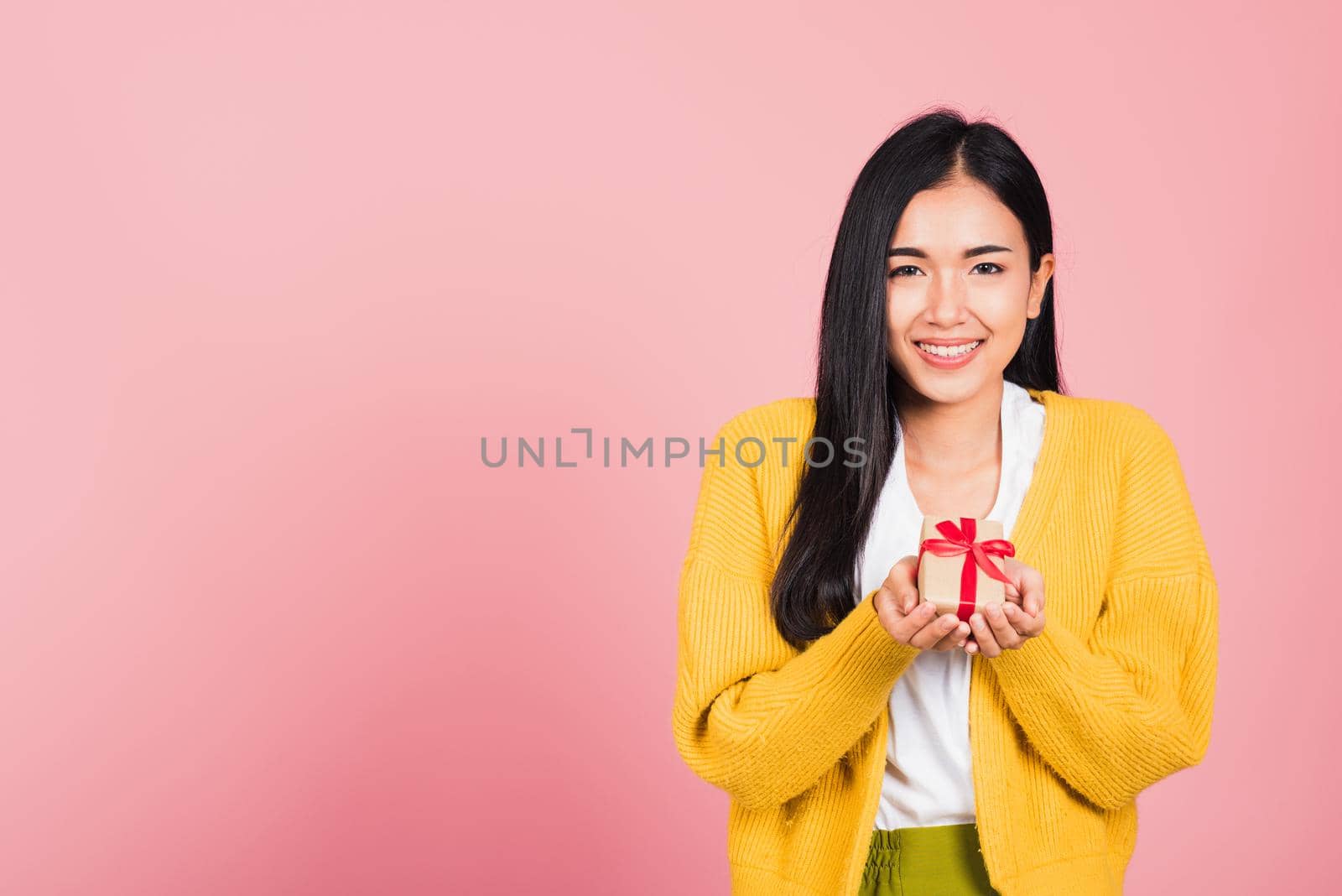Portrait of happy beautiful Asian young woman smiling holding small gift box on hands, studio shot isolated on pink background, Birthday, New year, Christmas, valentine, holiday day concept