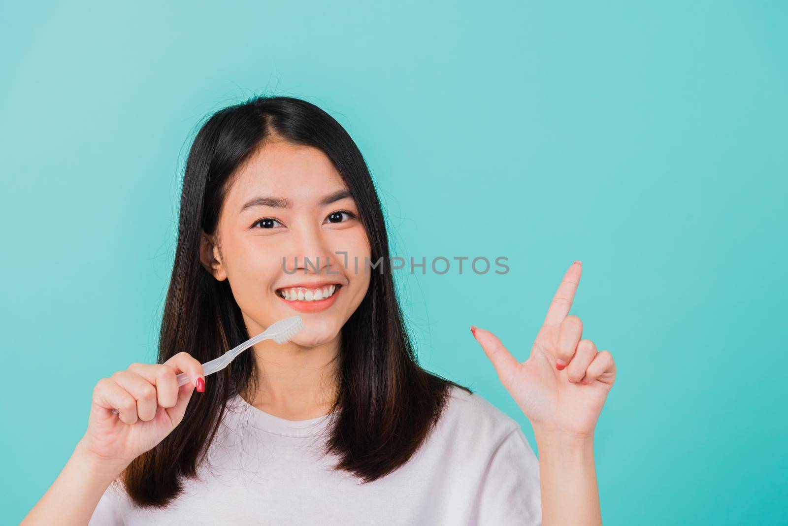 Portrait Asian beautiful young woman teen smiling holding toothbrush brushing teeth in the morning pointing finger to empty space studio shot isolated on blue background, Dental health concept