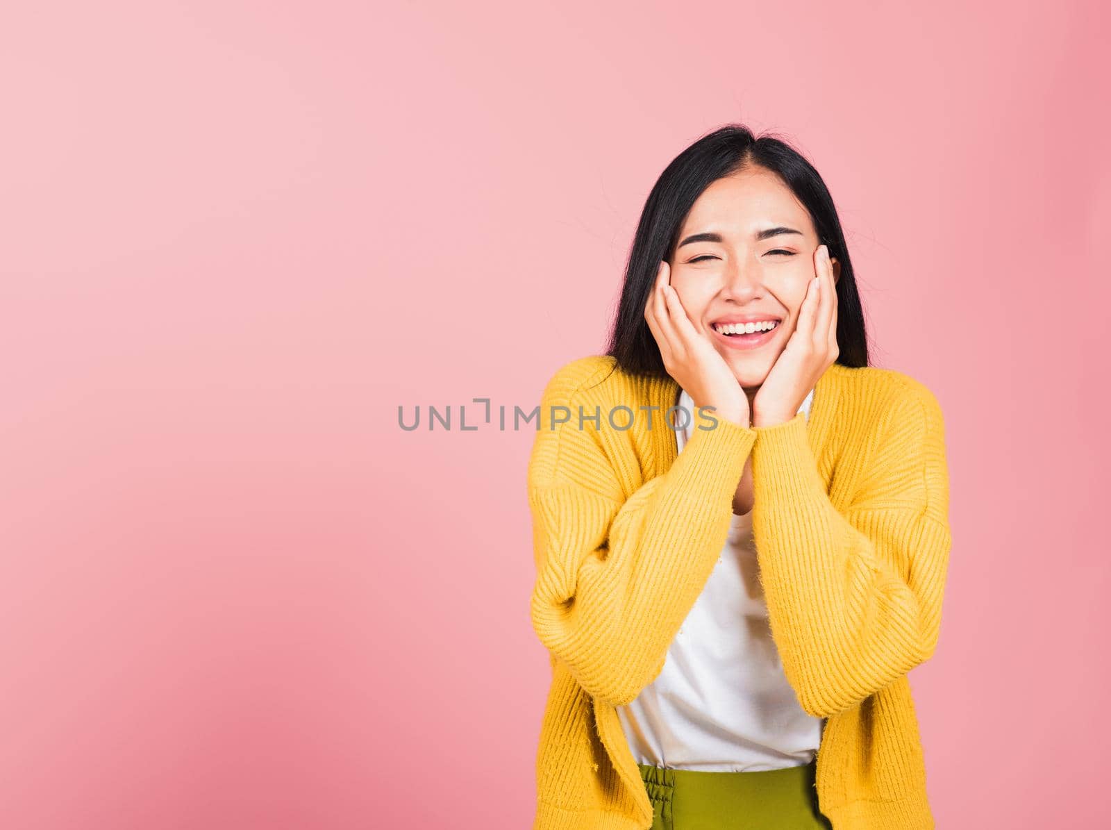 Happy Asian portrait beautiful cute young woman smile holding her cheeks looking to camera studio shot isolated on pink background Thai female beauty face touch massage healthy skin with copy space