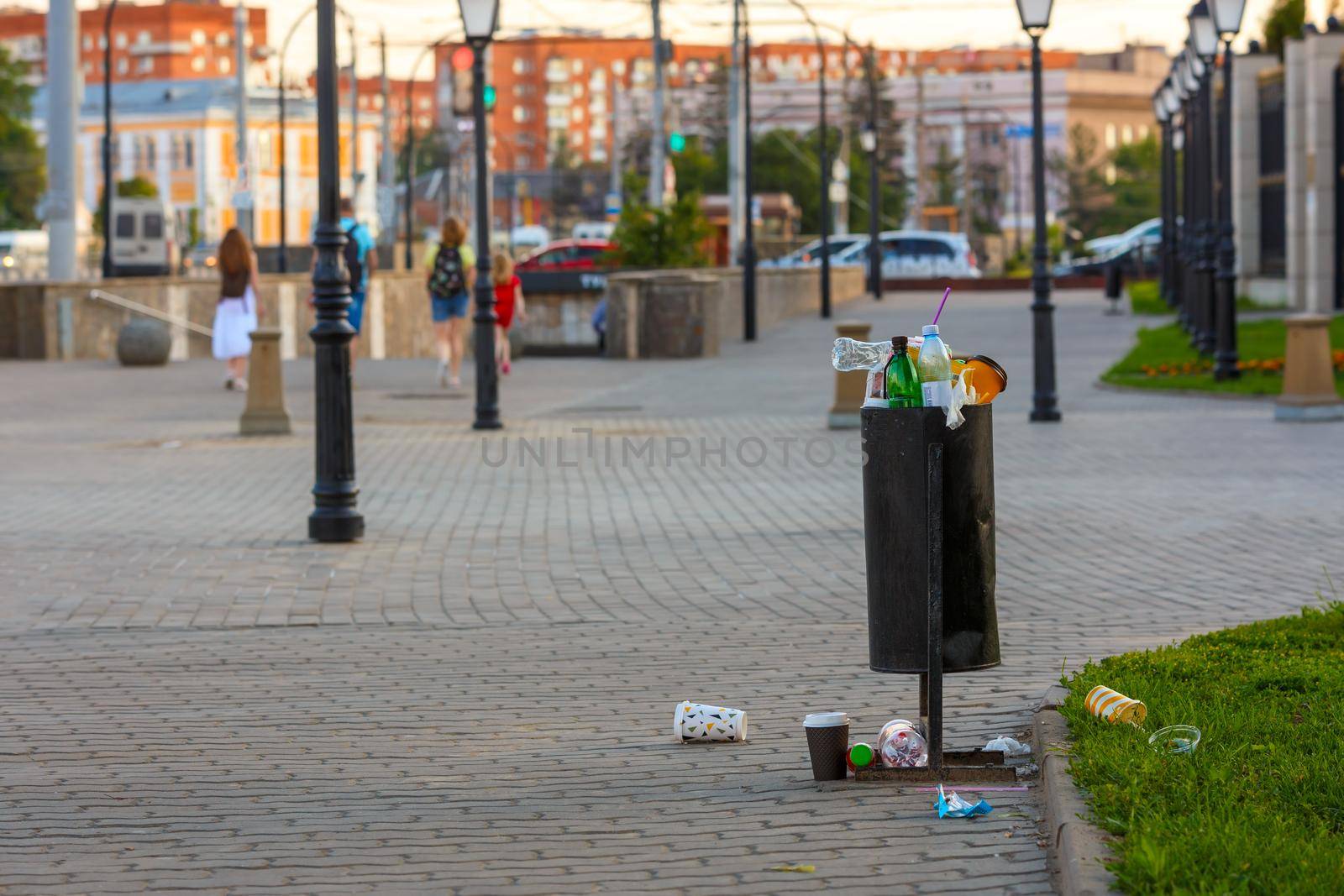 overflowing trash can on the sidewalk pavement at summer daylight.