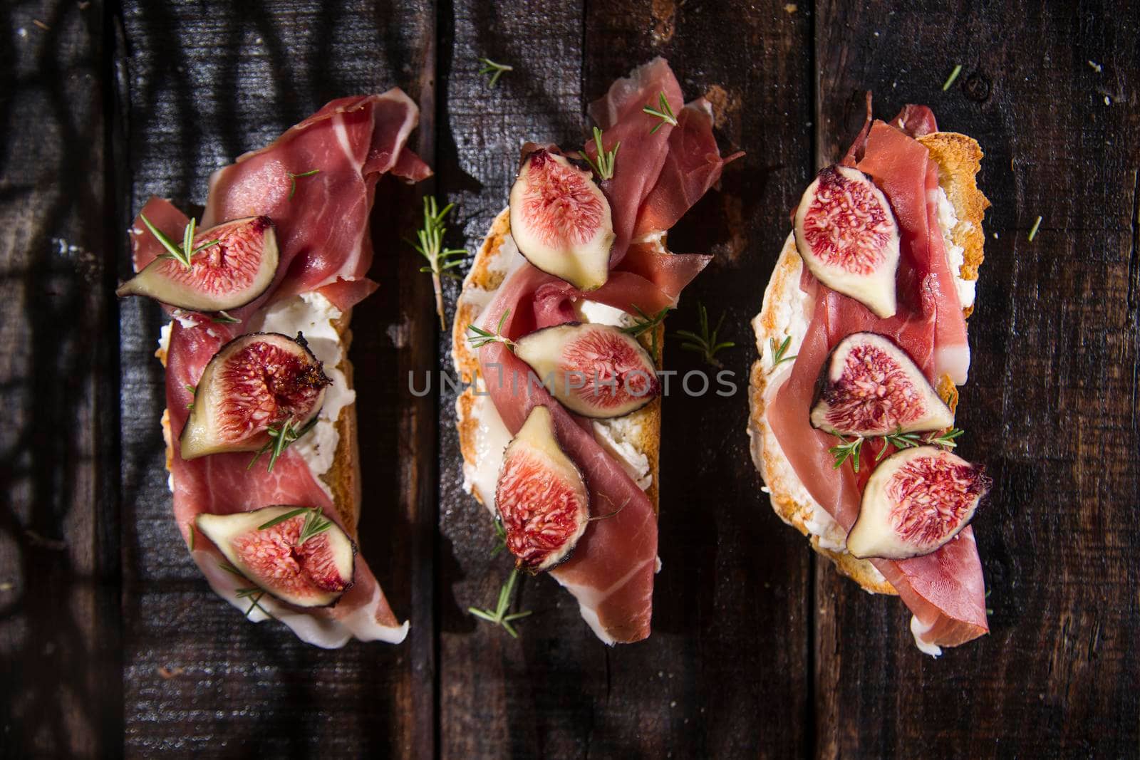 Presentation on wooden table bruschetta with figs and prosciutto